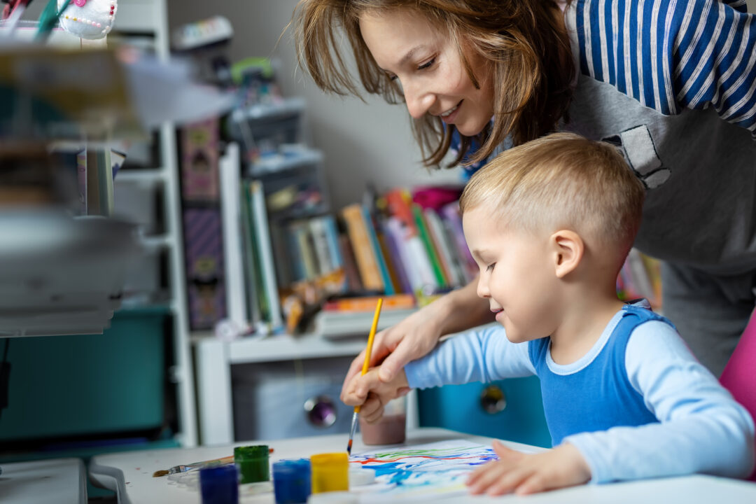 Young adult mom with a cute little boy enjoying and having fun painting with watercolor brush.