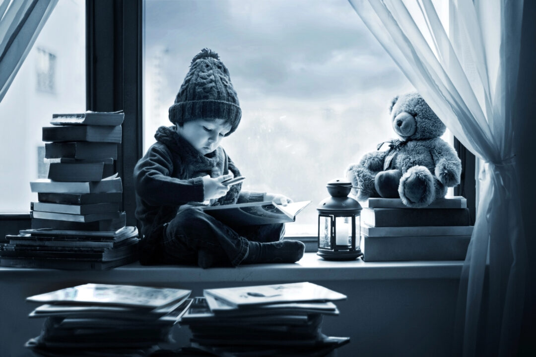 A little boy writing a letter, surrounded by stacks of books