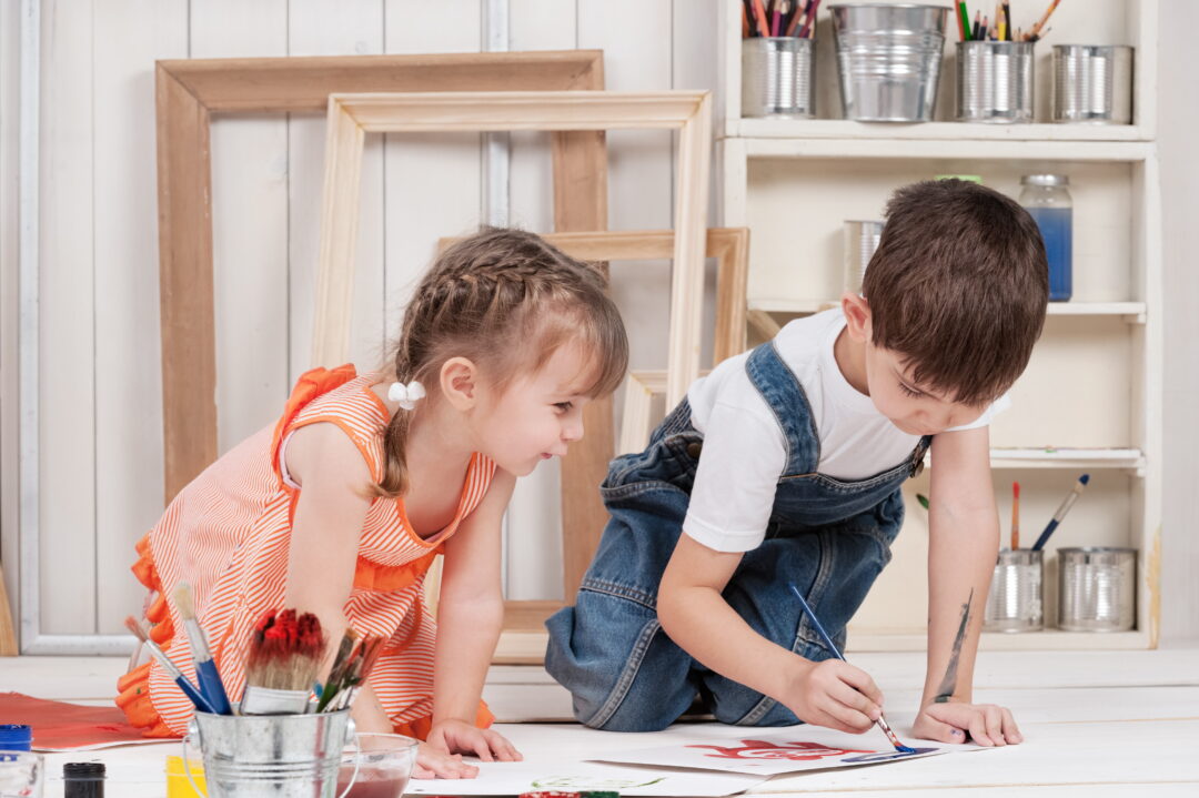 A little girl and a little boy having fun painting with watercolors.